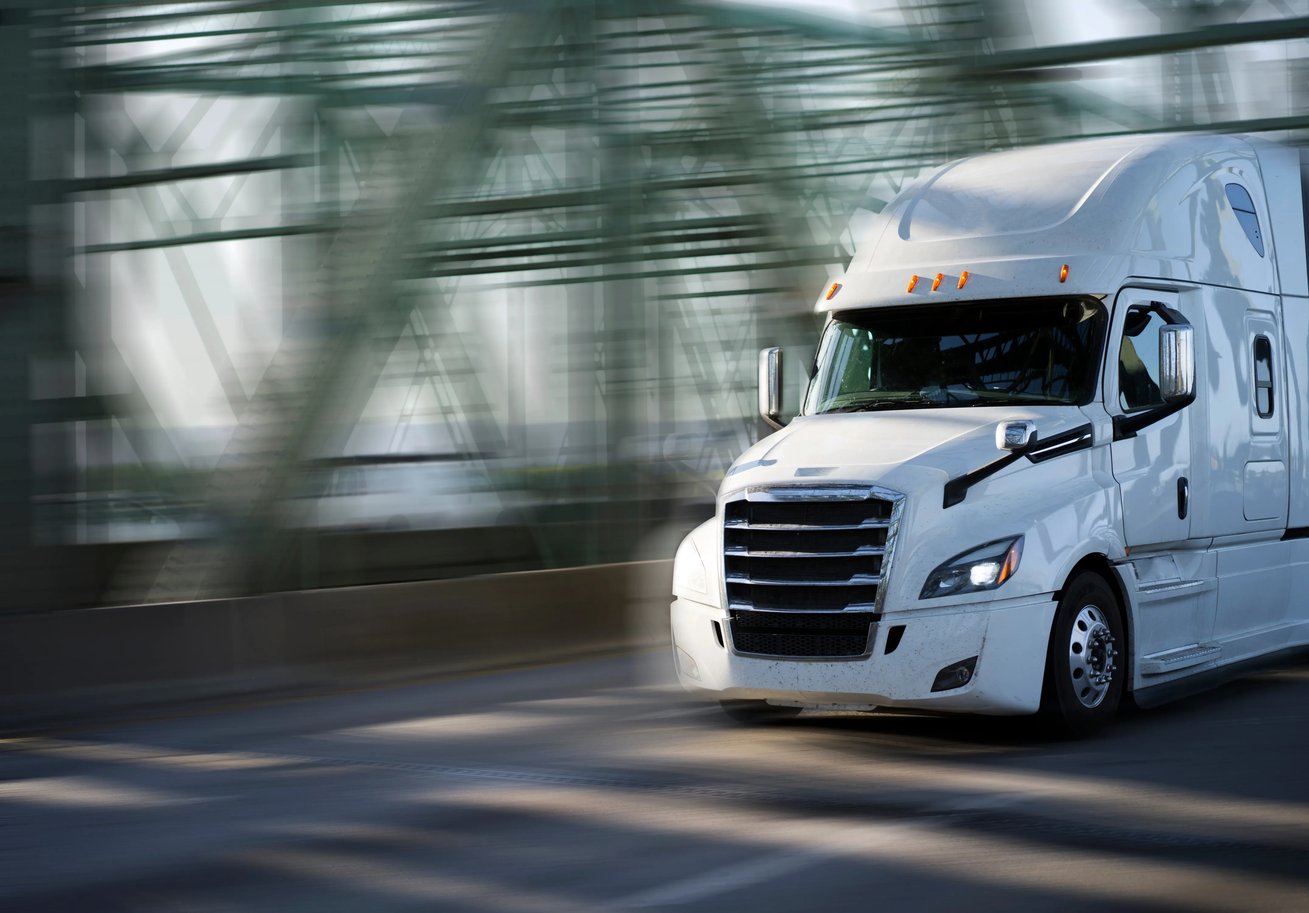 A white sleeper tractor crossing a steel bridge, the girders blurred with speed.